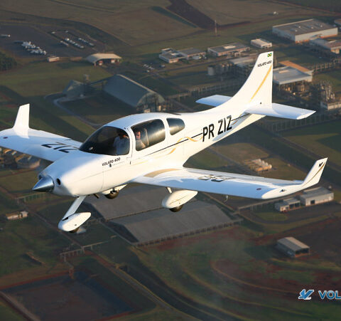 A small white plane flying over the grass.
